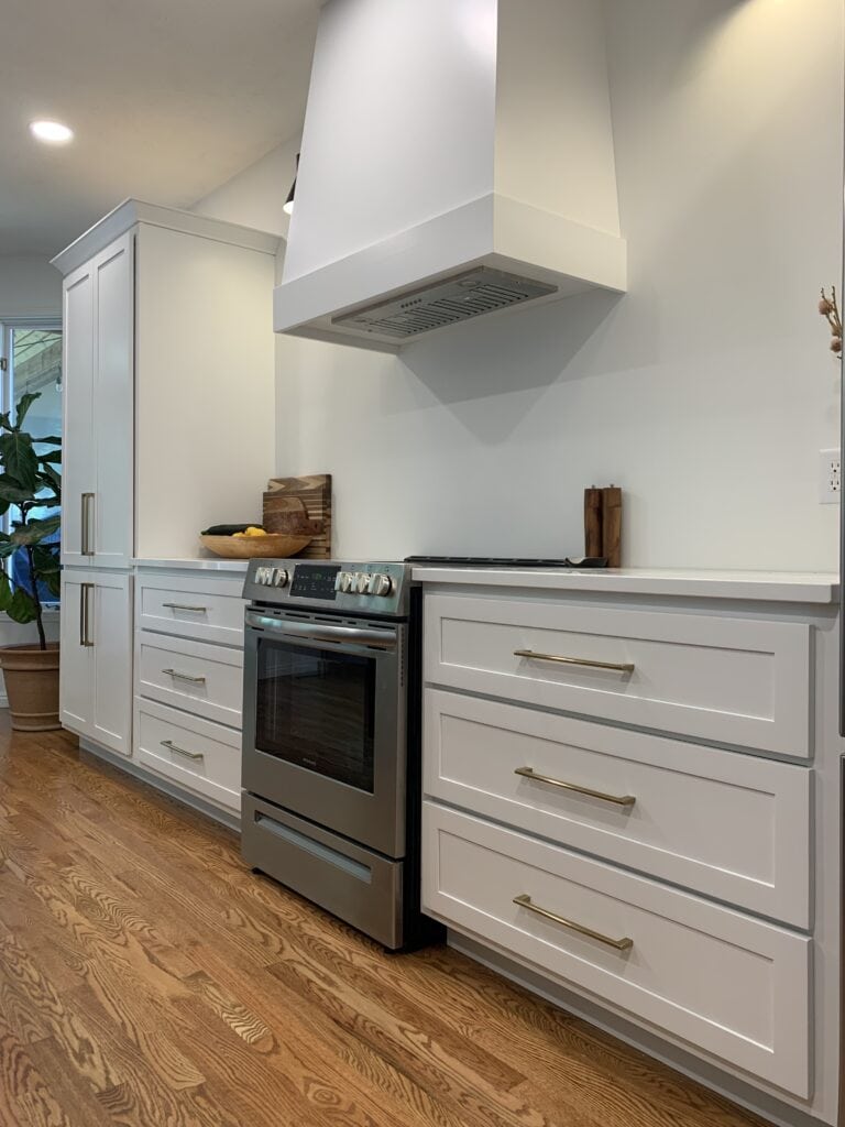 Modern white kitchen cabinets with sleek gold handles and stainless steel stove.