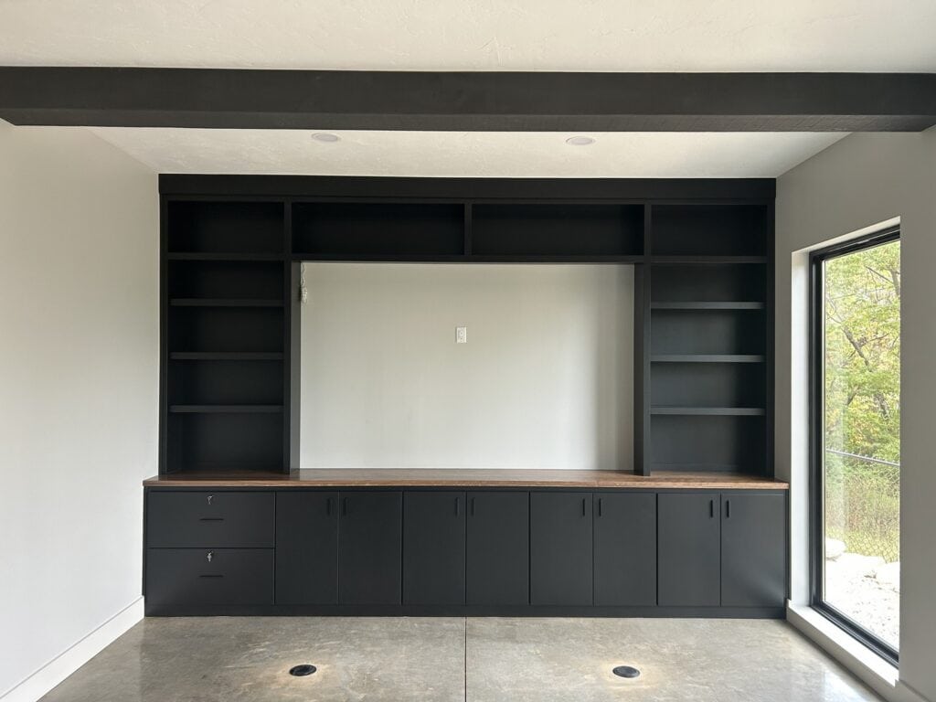 Front view of a sleek black cabinet unit with brass hardware and glass-front upper doors, showcasing interior lighting and display shelves.