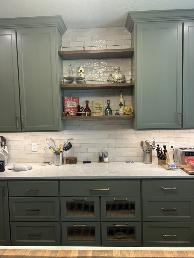 Close-up detail of sage green kitchen cabinets featuring open natural wood shelving with under-cabinet lighting and decorative items.