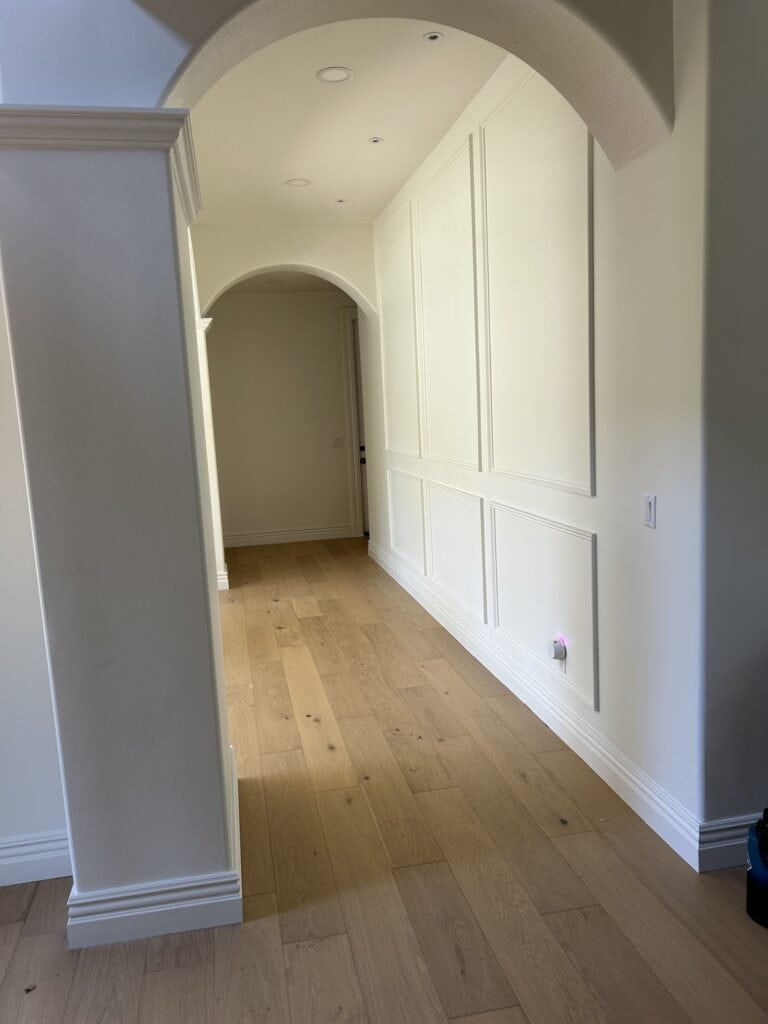 An elegant hallway lined with white wainscoting and featuring architectural arches leading to adjacent rooms.