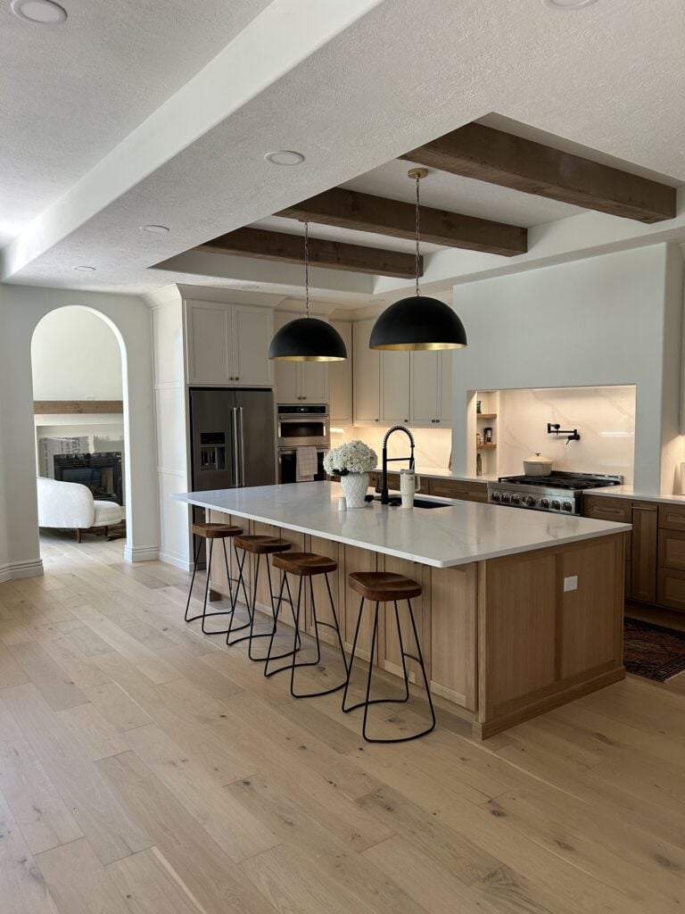 Wide shot of a spacious kitchen featuring a large central island, vaulted ceilings with exposed wooden beams, and pendant lighting.